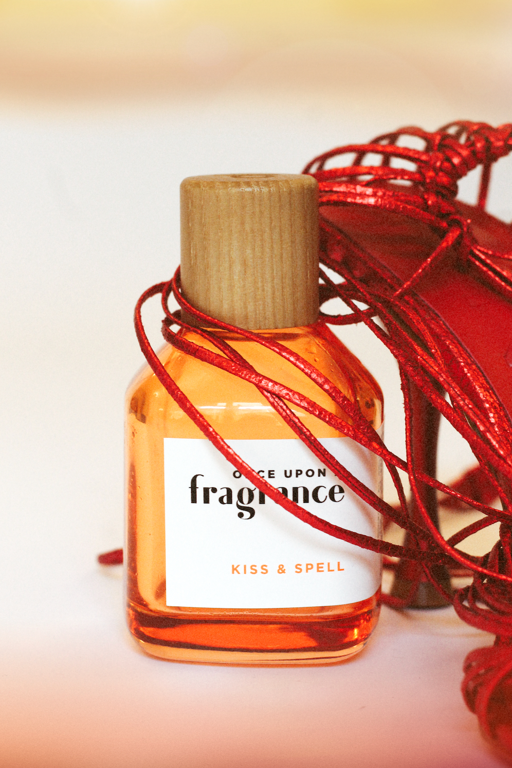 KISS & SPELL fragrance bottle by Once Upon a Fragrance wrapped around red women’s heels, showcasing a premium, seductive designer scent with notes of red berries, rose vanilla, and tonka