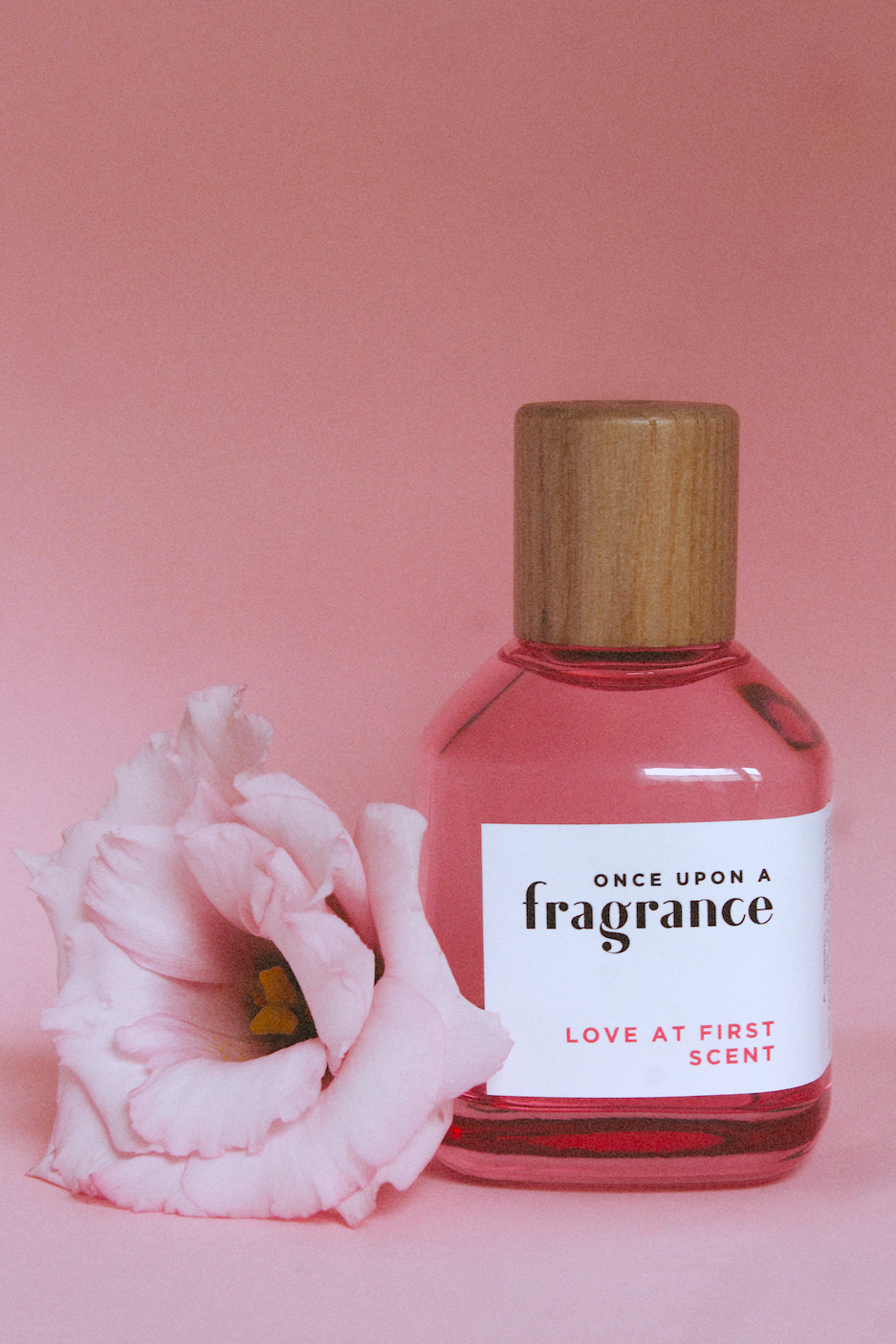 LOVE AT FIRST SCENT fragrance bottle by Once Upon a Fragrance in a pink environment with a flower, highlighting a premium, long-lasting French perfume with fruity and floral notes