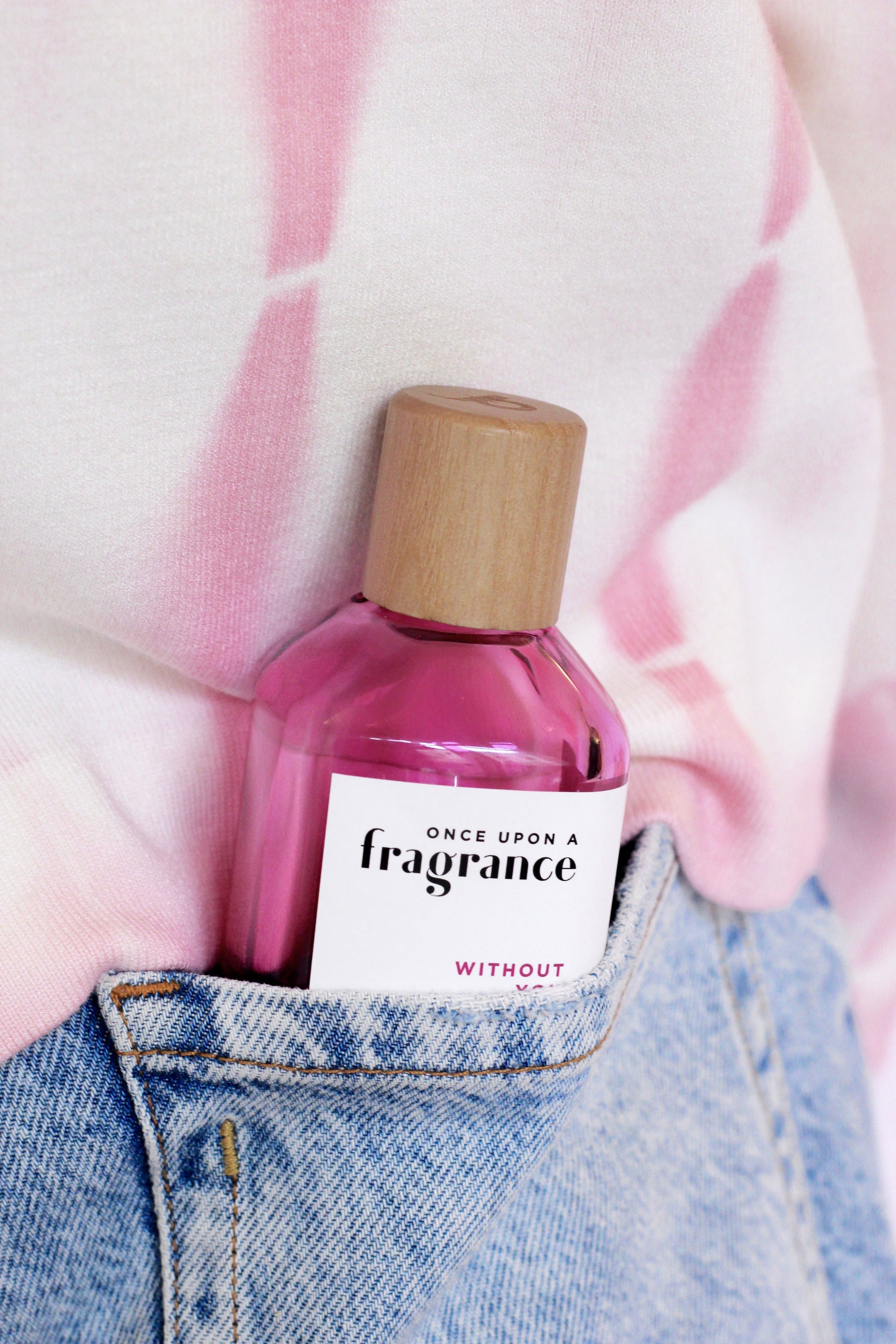 WITHOUT YOU fragrance bottle by Once Upon a Fragrance in a pink environment near the back pocket of a woman, showcasing a premium, long-lasting French perfume with cherry, floral, and amber-musk notes.
